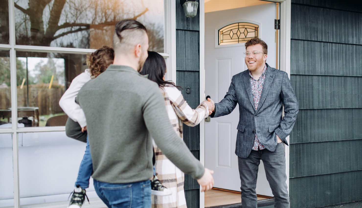 A smiling residential real estate agent stands at an open front door