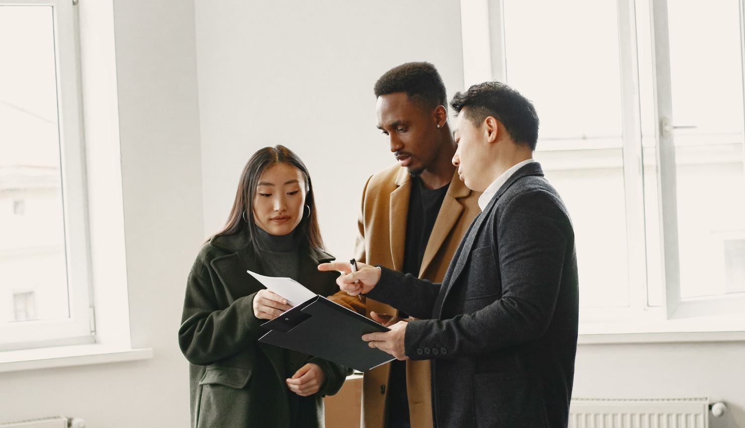 A real estate agent reviews a clipboard document with a young couple
