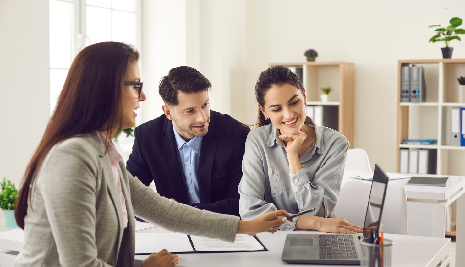 A female professional points at a laptop screen during a meeting