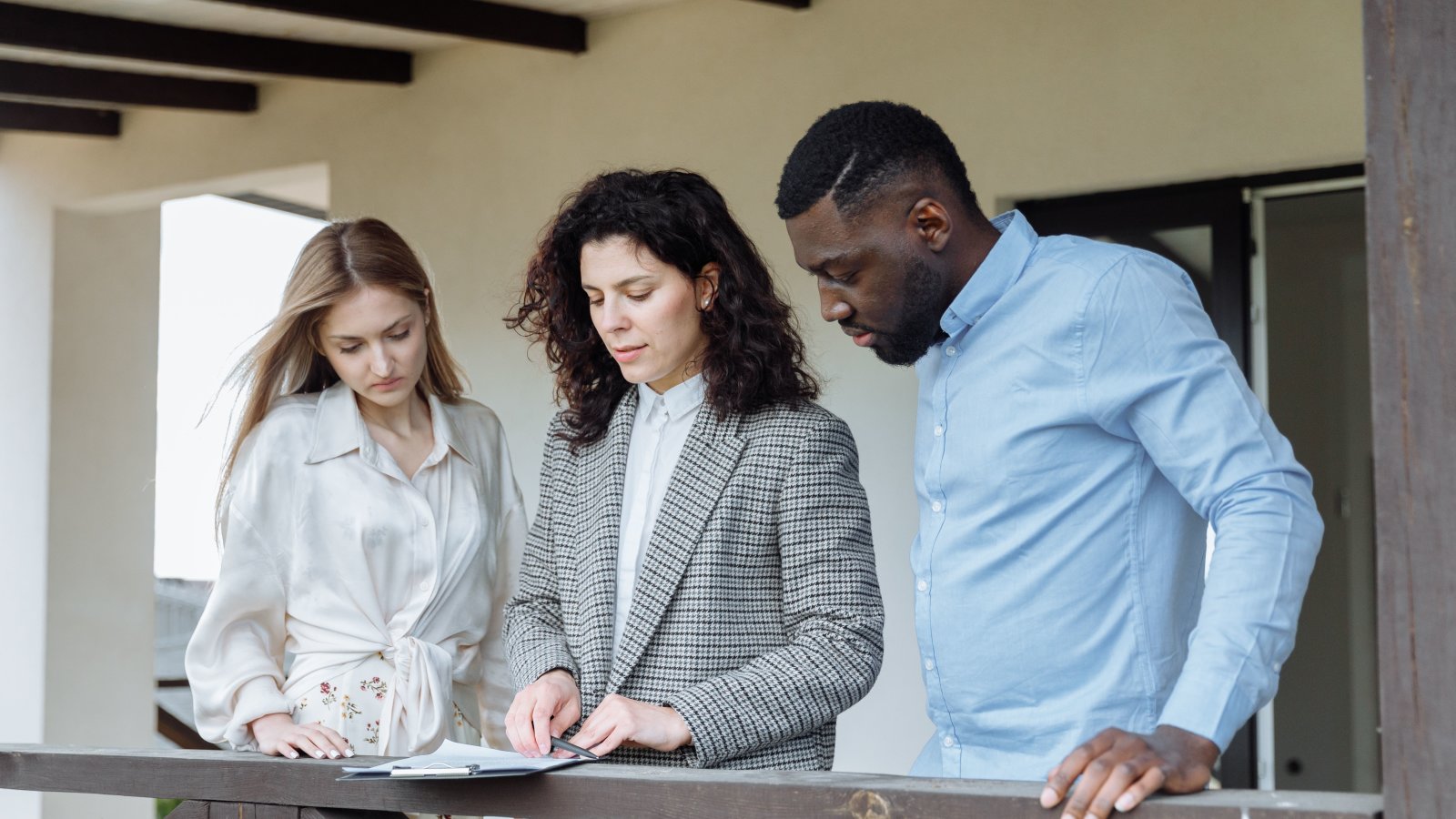 Three adults reviewing documents on a balcony during a real estate consultation